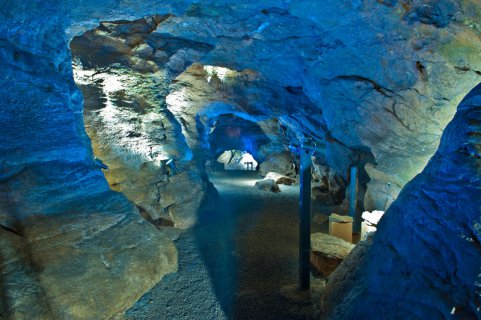 Ein Weg, der tief in die Höhle hineinführt. Scheinwerfer strahlen die nackten Felsen mit blauem Licht an.