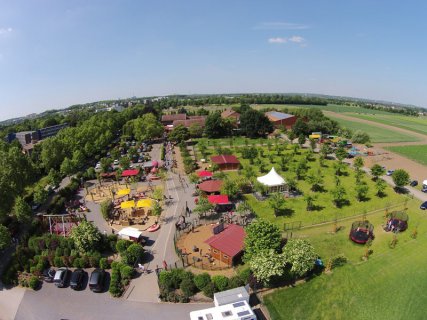 Ein Blick von oben auf das Gelände des Getrudenhofs. Mit Wiesen, Obstbäumen, Ställen, Spielplatz und Sonnenschirmen und einem Parkplatz vor dem Eingang.