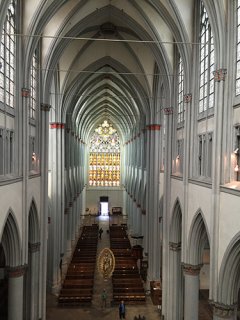 Im Mittelschiff des Doms befinden sich Gebetsbänke. Im Hintergrund leuchtet ein prächtiges Glasfenster über dem Eingangsportal.