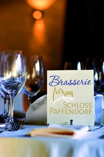 Auf einem frisch gedeckten Tisch steht eine Speisekarte der Brasserie Schloss Pfaffendorf.