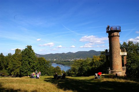 Ein mittelalterlicher Aussichtsturm mit Blick ins Rheintal bei bestem Wetter. Mehrere Besuchergruppen sind unterwegs.