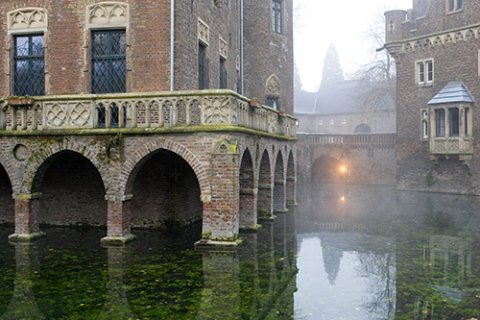 Grün-leuchtendes Wasser reicht bis an die Mauern des Schlosses heran. Die nebelige Szenerie erinnert ein bisschen an Venedig.