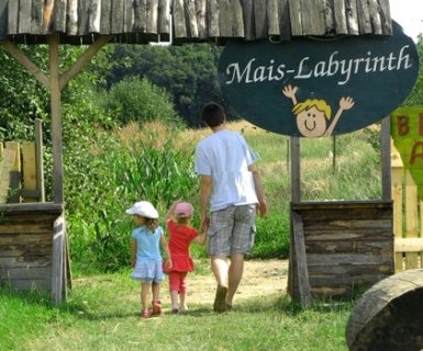 Ein Vater geht mit zwei kleinen Mädchen durch den Eingang zum Mais-Labyrinth. Ein Mädchen zeigt aufgeregt in Richtung Maisfeld.