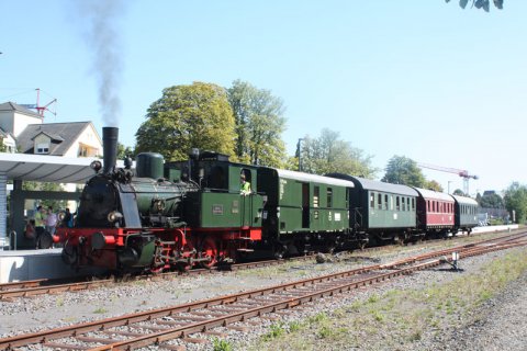 Eine grüne Dampflok mit vier Waggons hält an einem Bahnsteig.