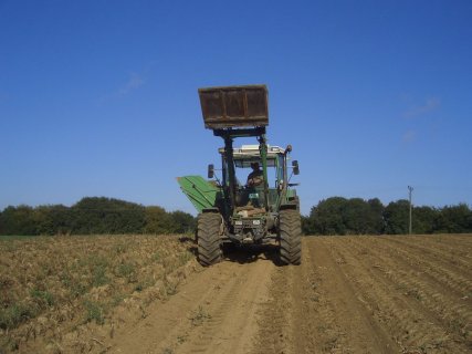 Ein Traktor mit erhobener Schaufel fährt über ein karges Feld und sät aus. 