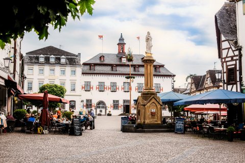 Der Linzer Marktplatz mit Kopfsteinpflaster, Außengastronomie, einer Mariensäule und im Hintergrund das historische Rathaus sowie links hinten ein großes, historisches Doppelhaus.