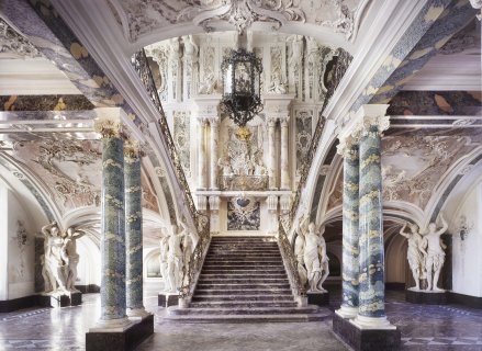 Prunktreppe von Balthasar Neumann im Saal von Schloss Augustusburg. Drumherum sind vier Marmorsäulen, an den Wänden kunstvoller Stuck. 