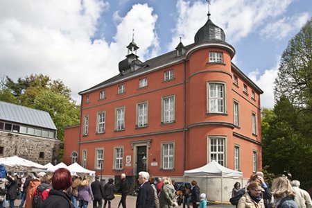 Ein Blick von außen auf die rote Fassade des Museums im Schloss Wissem. Besucherinnen und Besucher stehen davor.